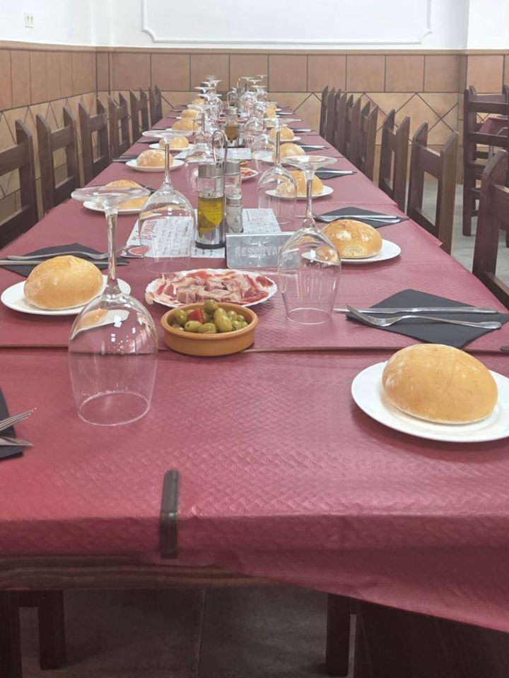 Mesa larga preparada para una celebración en el salón, con pan, jamón y aceitunas
